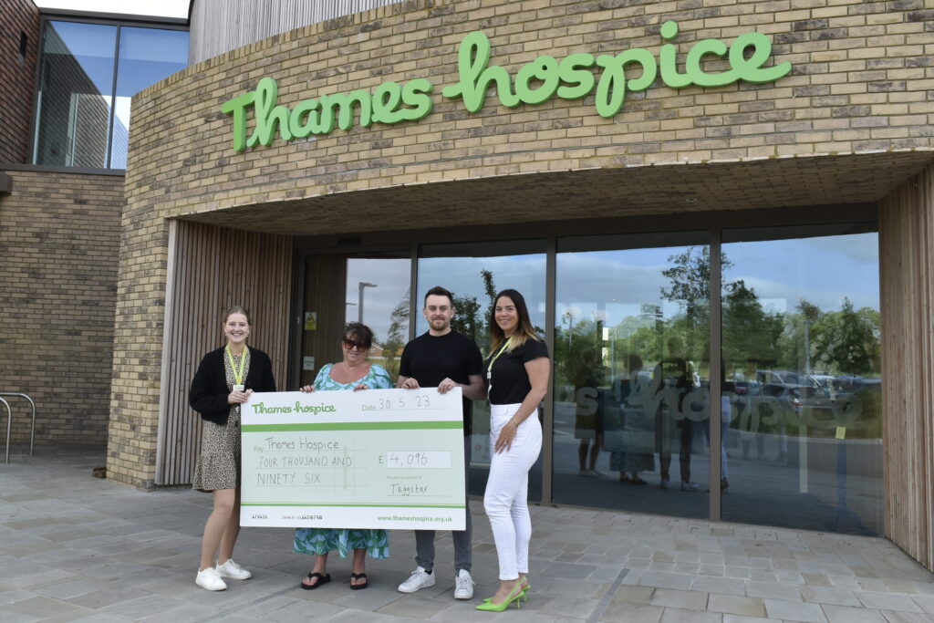 Four people being photographed with a cheque donation of £4,096 outside of the Thames Hospice building