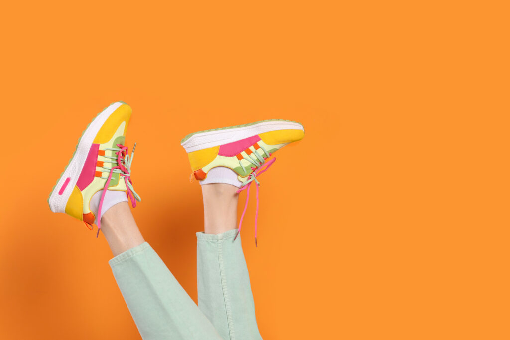 Woman wearing pair of new stylish sneakers on orange background, closeup
